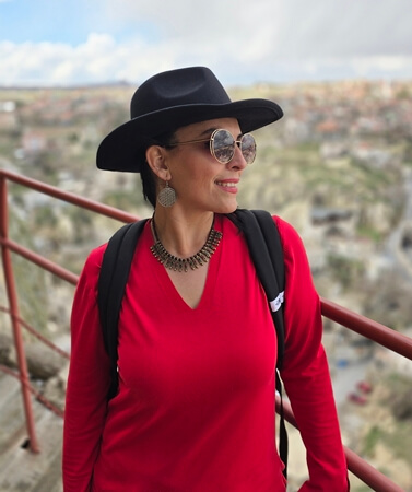 Ortahisar manzarasına karşı poz veren kırmızı kıyafetli bir gezgin; Kapadokya vadileri arka planda